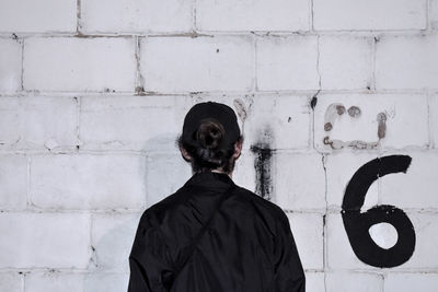 Rear view of man with hair bun standing by white wall