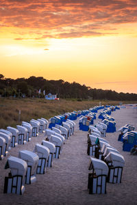 Empty chairs on beach against sky during sunset