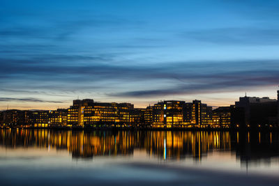 Scenic view of river by illuminated buildings against sky at sunset