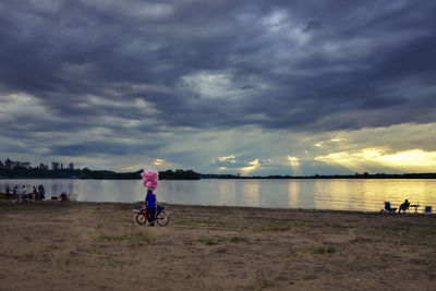 Man riding bicycle on beach against sky during sunset