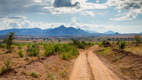 Dirt road amidst landscape against sky