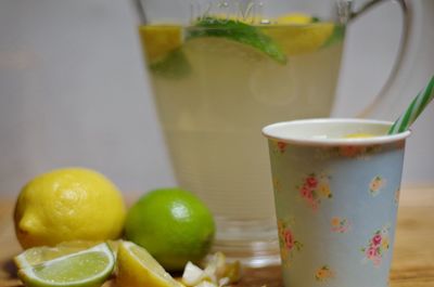 Close-up of disposable cups with fresh lemonade in glass jug against wall