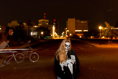 Portrait of young woman standing in illuminated city at night