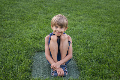 Portrait of boy sitting on stone amidst grass