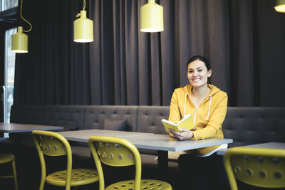 Portrait of smiling mid adult businesswoman with book in office cafeteria