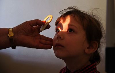 Cropped hand examining eyes of girl against wall