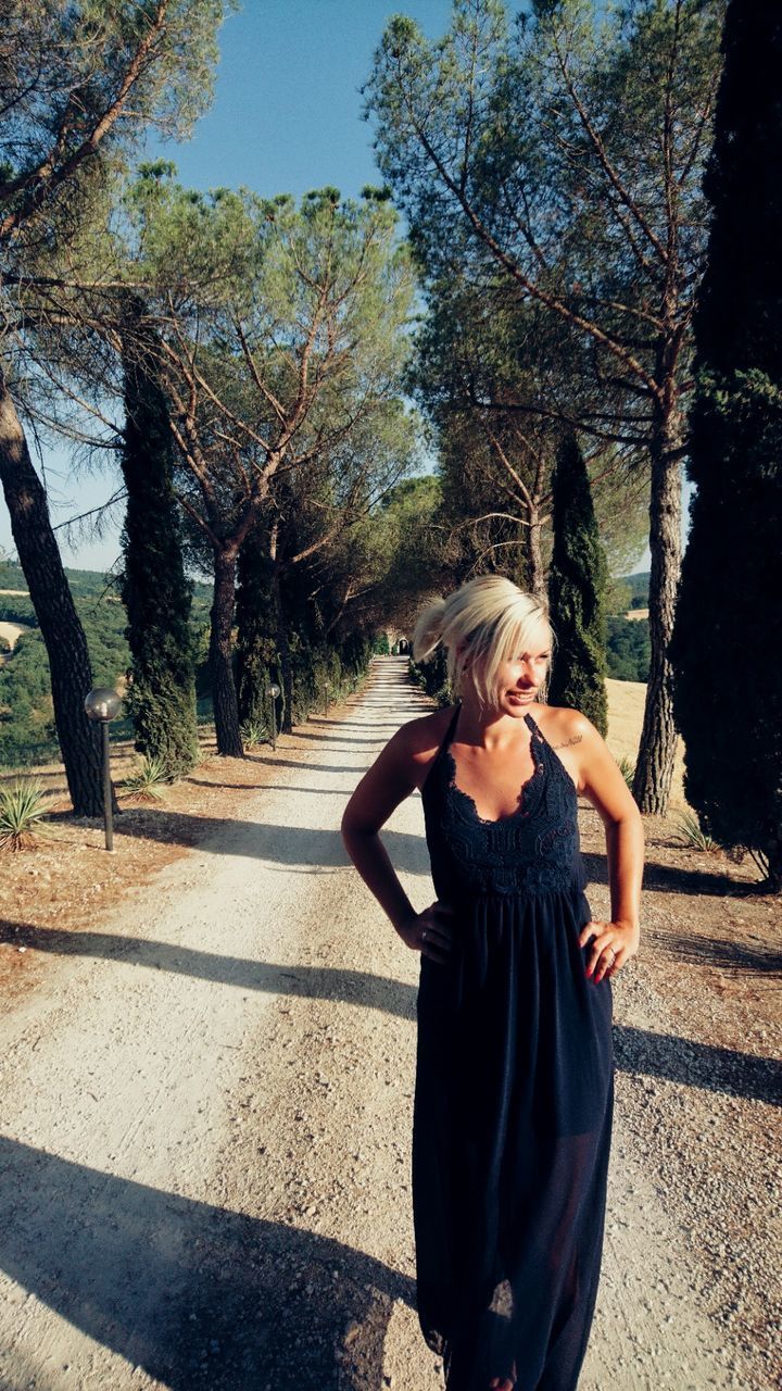 YOUNG WOMAN STANDING ON TREE TRUNK AGAINST TREES