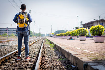 Rear view of young man with backpack standing on railroad track against clear sky