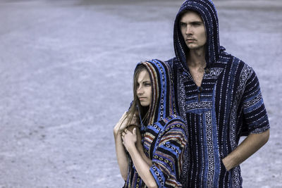 Thoughtful young couple wearing patterned hooded shirts on field