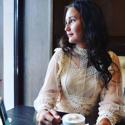 Portrait of young woman looking away while sitting on window