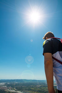 Rear view of man standing against sky on sunny day