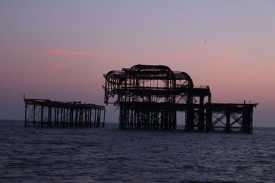 Broken metallic structure on sea against sky at dusk