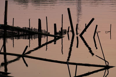 Wooden posts in lake against sky during sunset