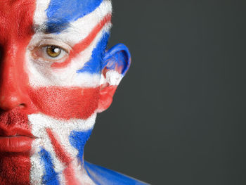 Close-up portrait of sad man with british flag body paint against black background