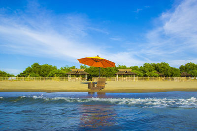 Lounge chair with parasol at beach against blue sky