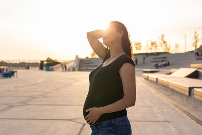 Side view of woman standing in city at sunset