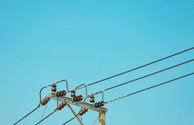 Low angle view of bird perching on cable against clear sky