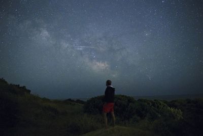 Rear view of man standing on field against stars at night