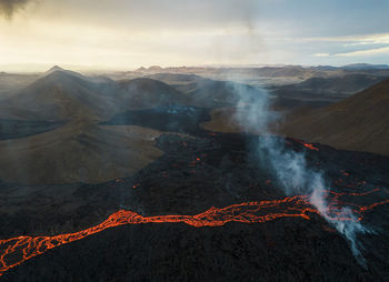 Drone view of stream of hot orange lava flowing through mountainous terrain in morning in iceland