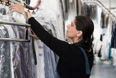 Side view of mature female dry cleaner by clothes rack at laundromat