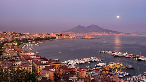 Aerial view of illuminated city by sea against sky