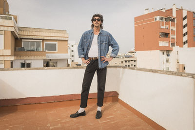 Fashionable man standing with arms akimbo on building terrace