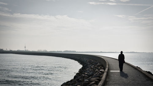 Silhouette person walking on pier in sea against during sunny day