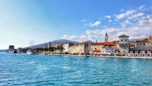 View of buildings by sea against blue sky