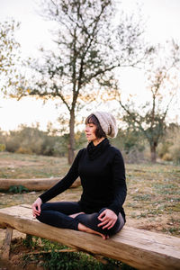 Woman sitting on plant against trees