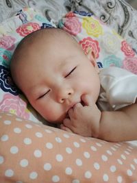 Cute baby girl with fingers in mouth sleeping on bed
