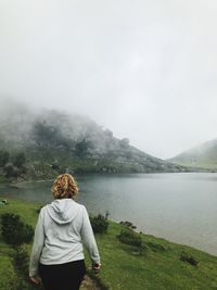 Rear view of woman walking at lakeshore against sky