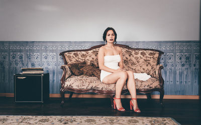 Full length of fashionable young woman sitting on chair against wall