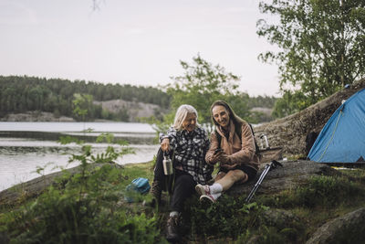 Senior female friends sharing smart phone while sitting on rock during camping