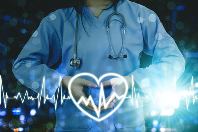 Midsection of man with heart shape standing against illuminated wall