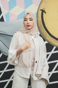 Portrait of young woman standing against wall