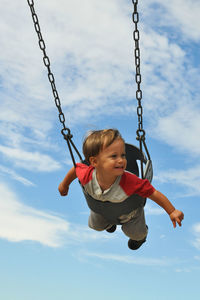 Low angle view of boy swinging against sky