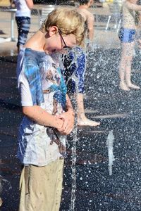 Side view of smiling boy with fountain water spraying on him