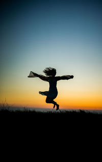 Silhouette woman jumping on field against sky during sunset