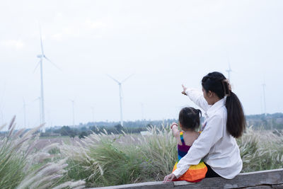 Beautiful young mother daughter relax sitting summer meadow background and windmill.