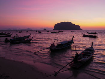 Boats moored in sea against sky during sunset