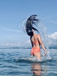Young woman splashing water in sea against sky
