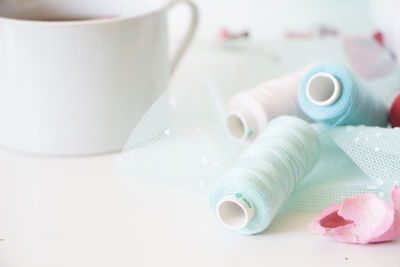 Close-up of thread spools and coffee on white table