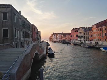 Canal passing through city against sky during sunset