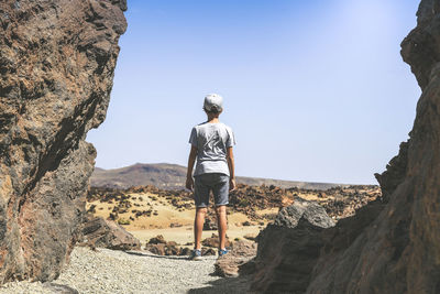 Rear view of boy standing on land against sky