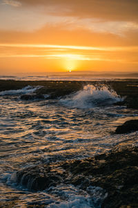 Image of the waves crashing on the rocks at sunset