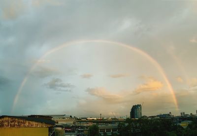 Rainbow over buildings in city against sky