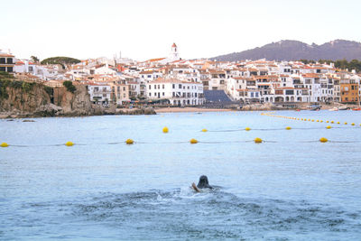 Woman swimming in sea against buildings