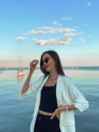 Young woman wearing sunglasses standing in sea against sky
