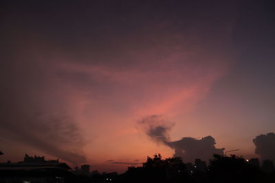 Silhouette trees against dramatic sky during sunset