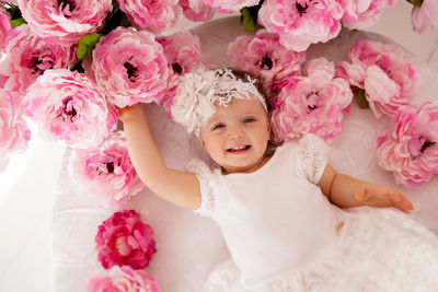 Baby girl lying on her stomach and smiles on the bed in clothes and a pink headband